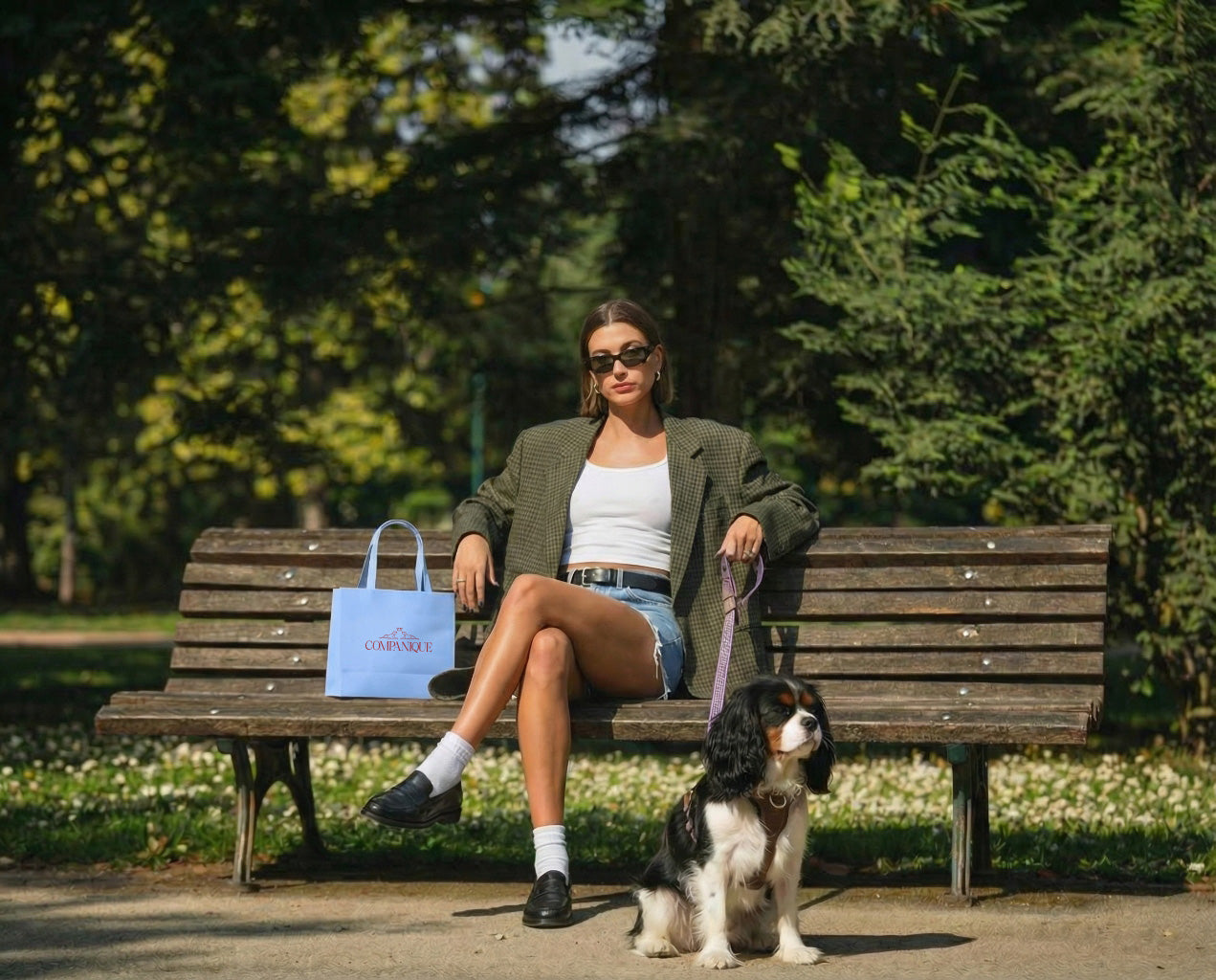 Woman sitting on a bench with a dog in a park, holding a blue bag.